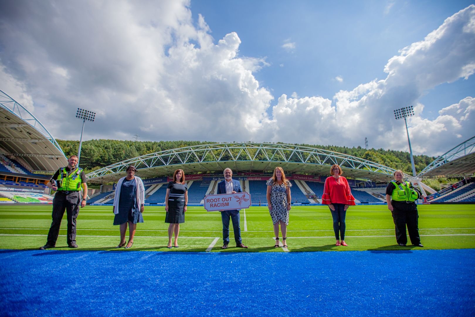 Cllr Pandor and others at Huddersfield Town Football Club stadium, holding a sign that says "Root Out Racism"