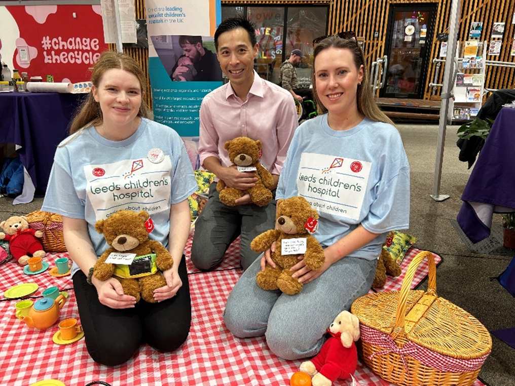 Three people smiling holding teddy bears with t shirts that say Leeds Children hospital