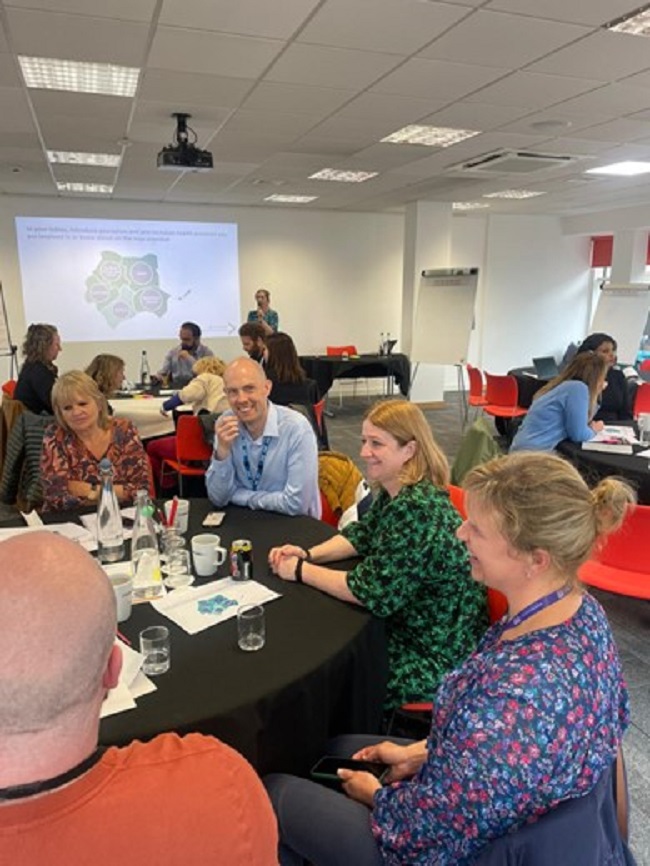 A group of attendees from an inclusion health meeting in August 2023 sitting at a round table