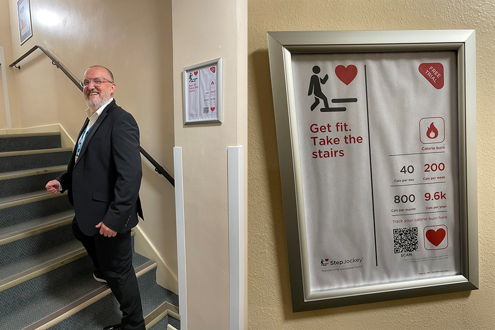 Man on stairs smiling next to poster that says "Get fit. Take the stairs".