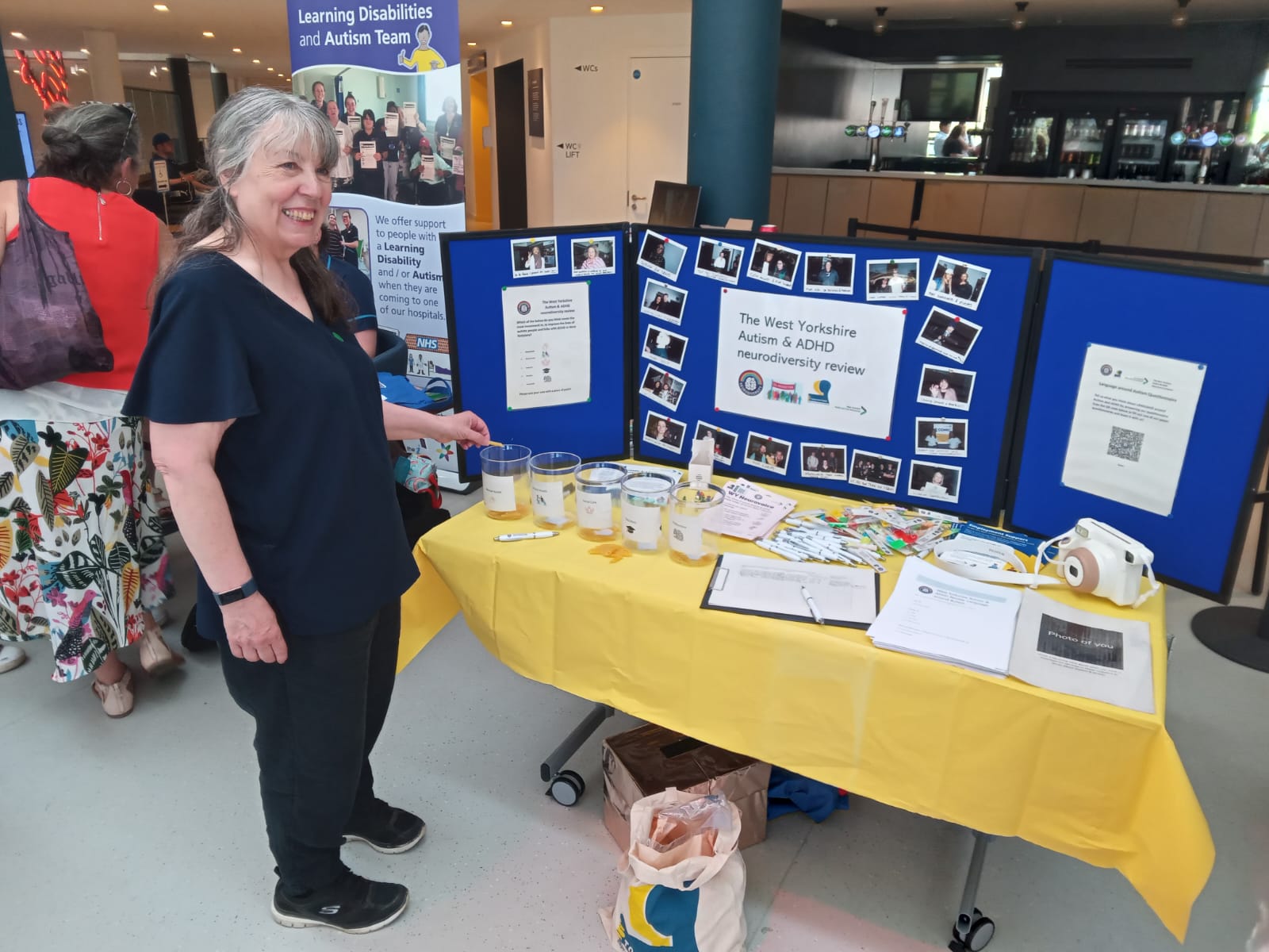 An image of a woman smiling in front of a pinboard which highlights the work done by the West Yorkshire Health and Care Partnership's neurodiversity programme.