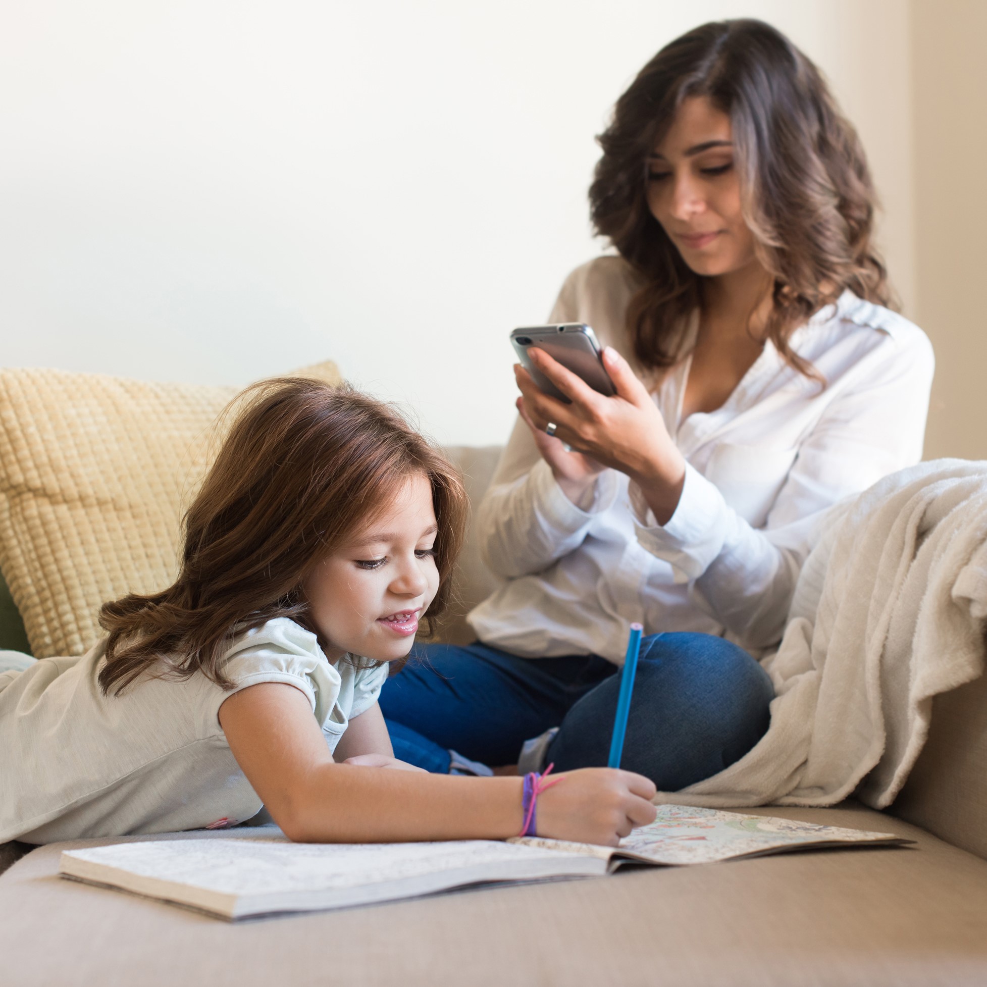 A young mum with her daughter. Mum is uploading a video on her smartphone