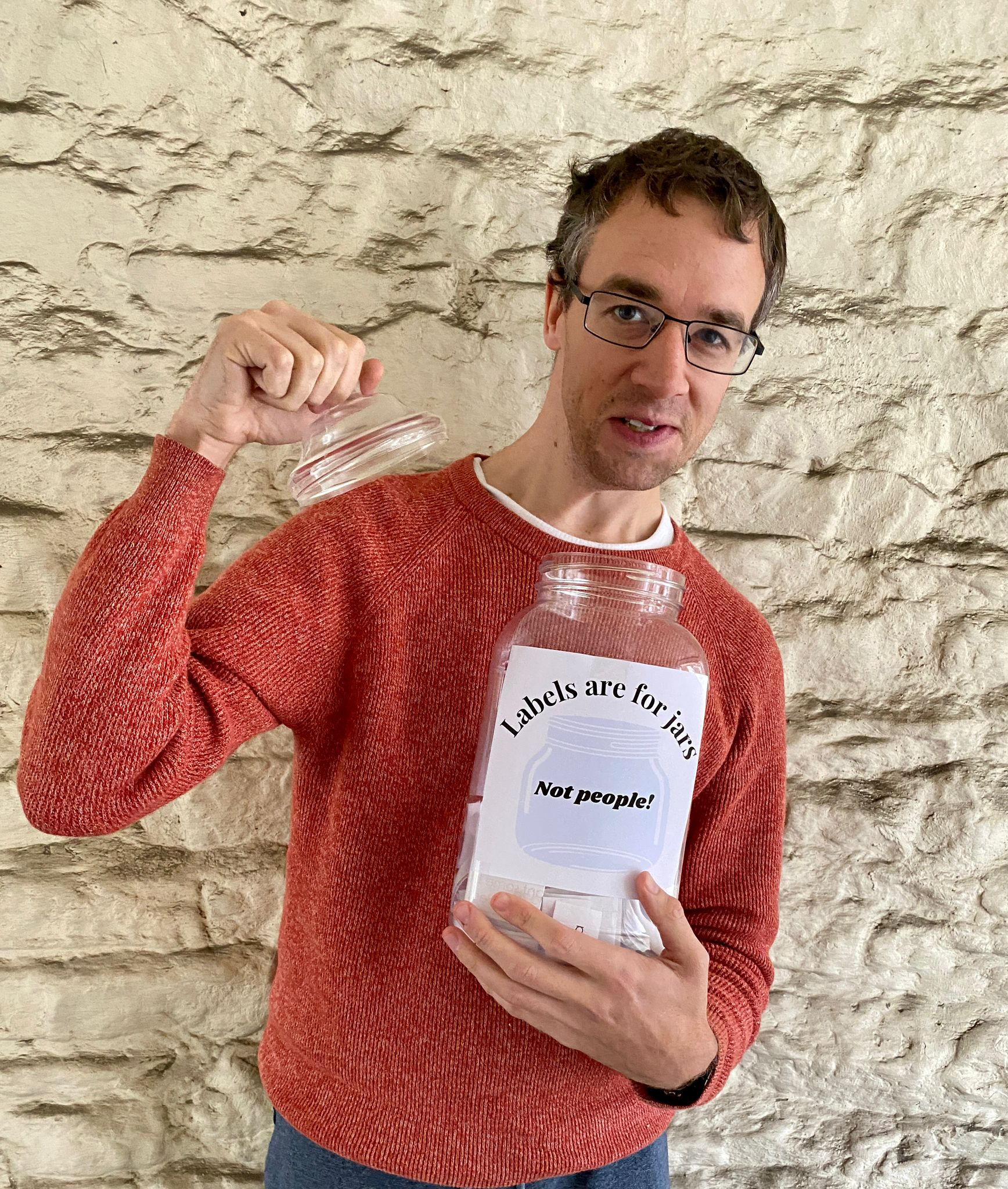 A man holding a glass jar in one hand and the lid in another. A label on the jar reads Labels are for jars. Not for people!