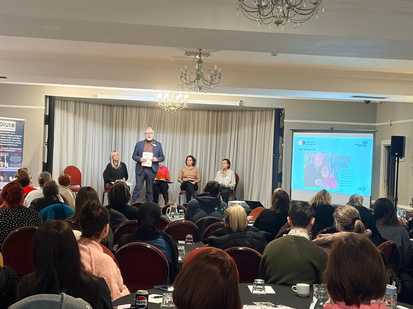 Delegates at tables and presenter at front 
