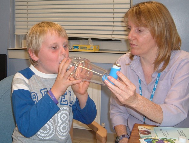 Child having an asthma attack, using a blue inhaler with spacer with adult supervision to relieve symptoms 