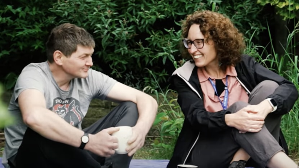 Image of two people sat in front of a bush