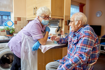 Reablement worker (masked) talking with man in his kitchen