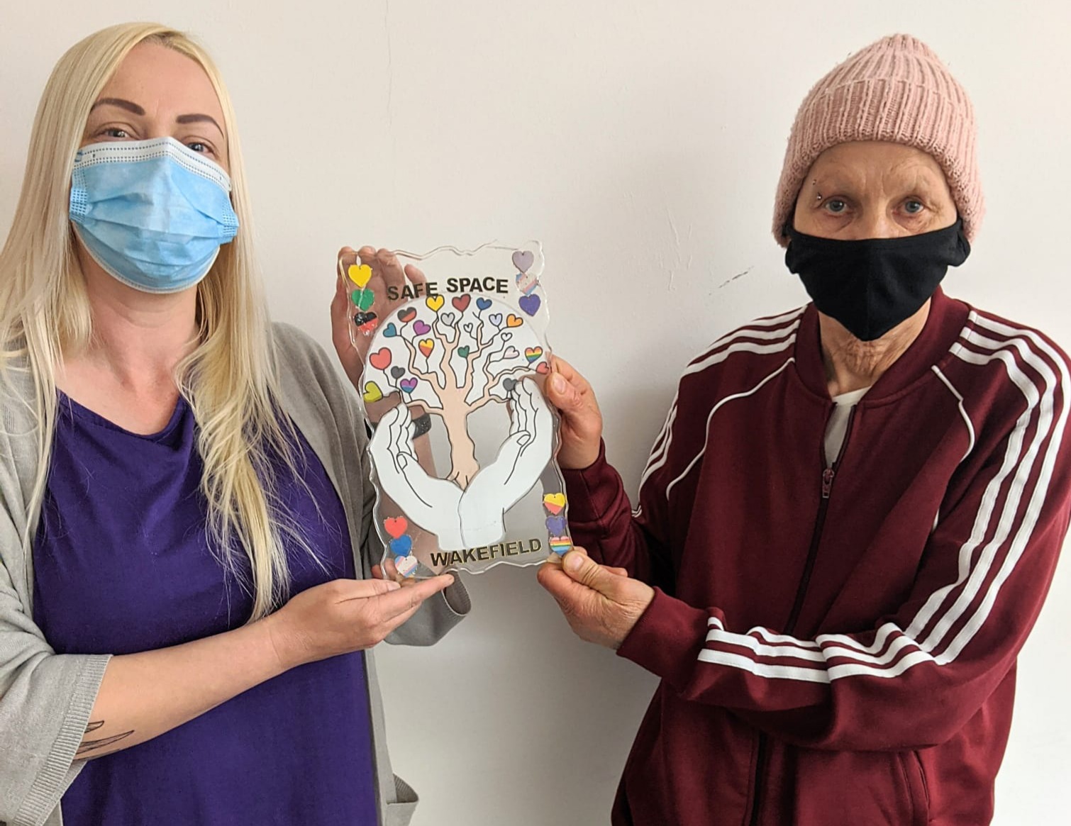 Two women in masks holding a Wakefield Safe Space artwork