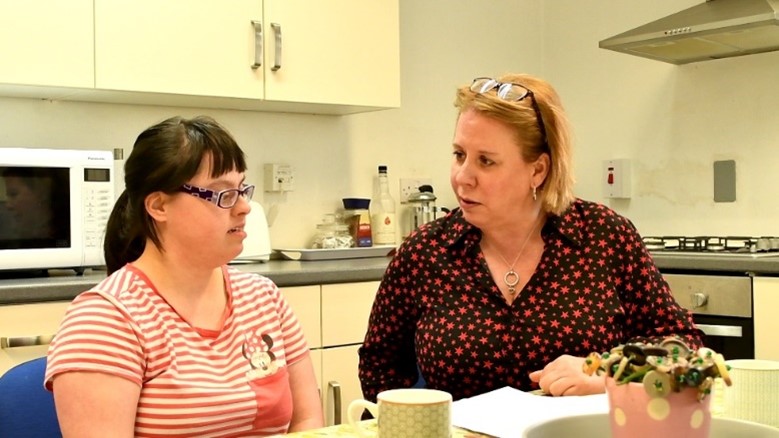 Photo of women sat at a kitchen table talking with a woman with learning disabilities