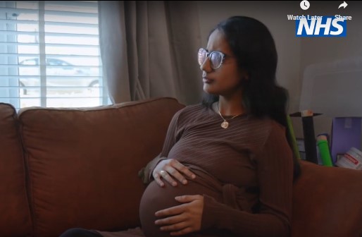 Pregnant woman sat on the sofa holding her belly