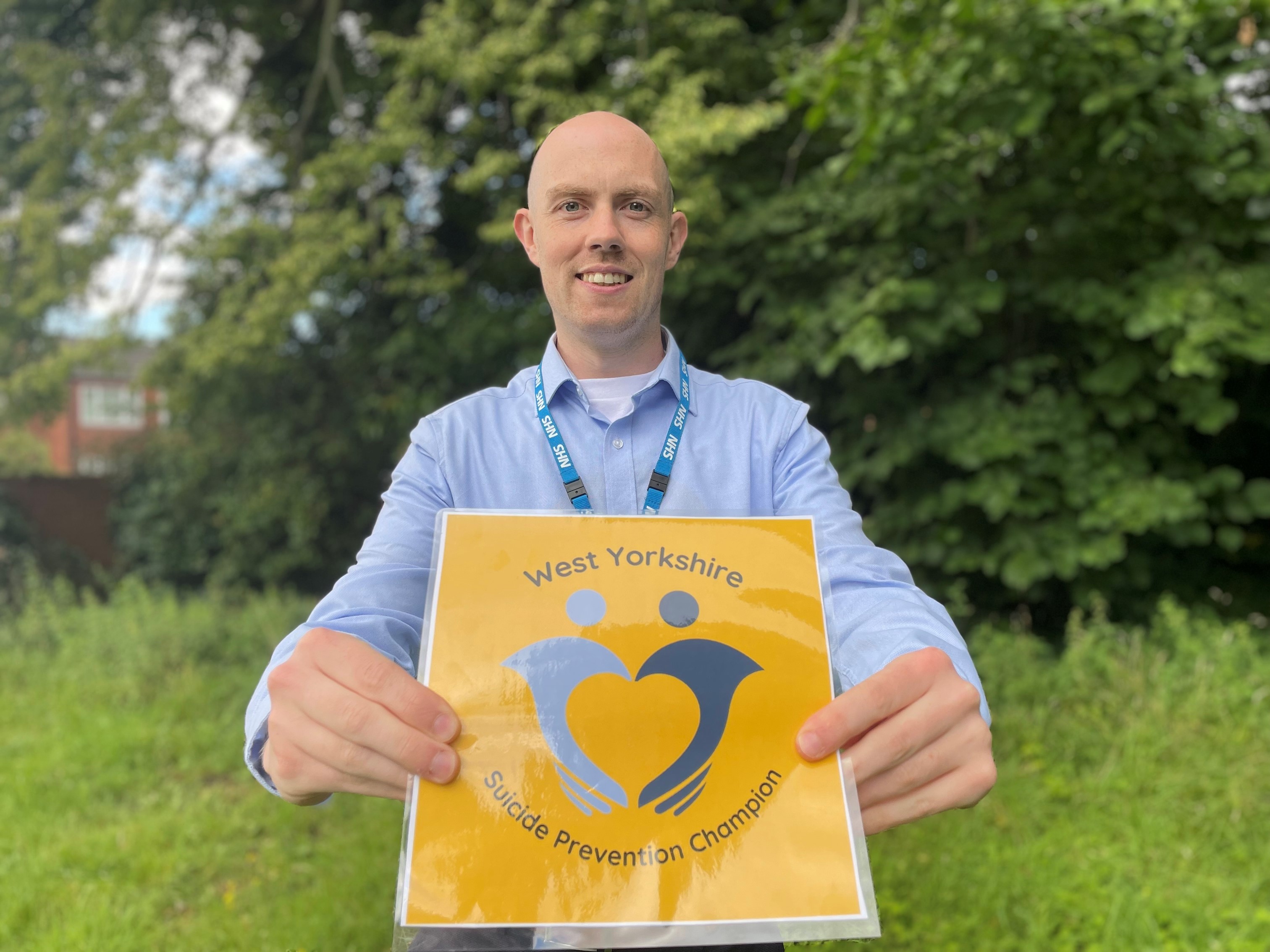 Image shows Richard James, WY HCP lead for Suicide Prevention work, holding a card with the Suicide Prevention Champions logo.jpg