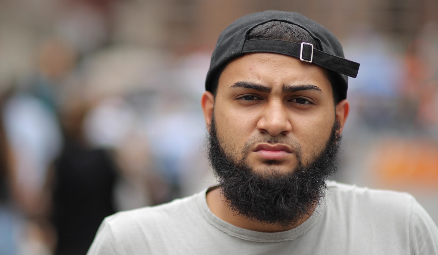 Photograph of a young man of Asian heritage. He has a beard, is wearing a baseball cap and is looking anxious.