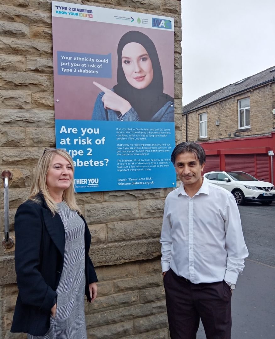 Adele Brearton and Sajeed Mahmood in front of a wall-mounted Type 2 diabetes poster